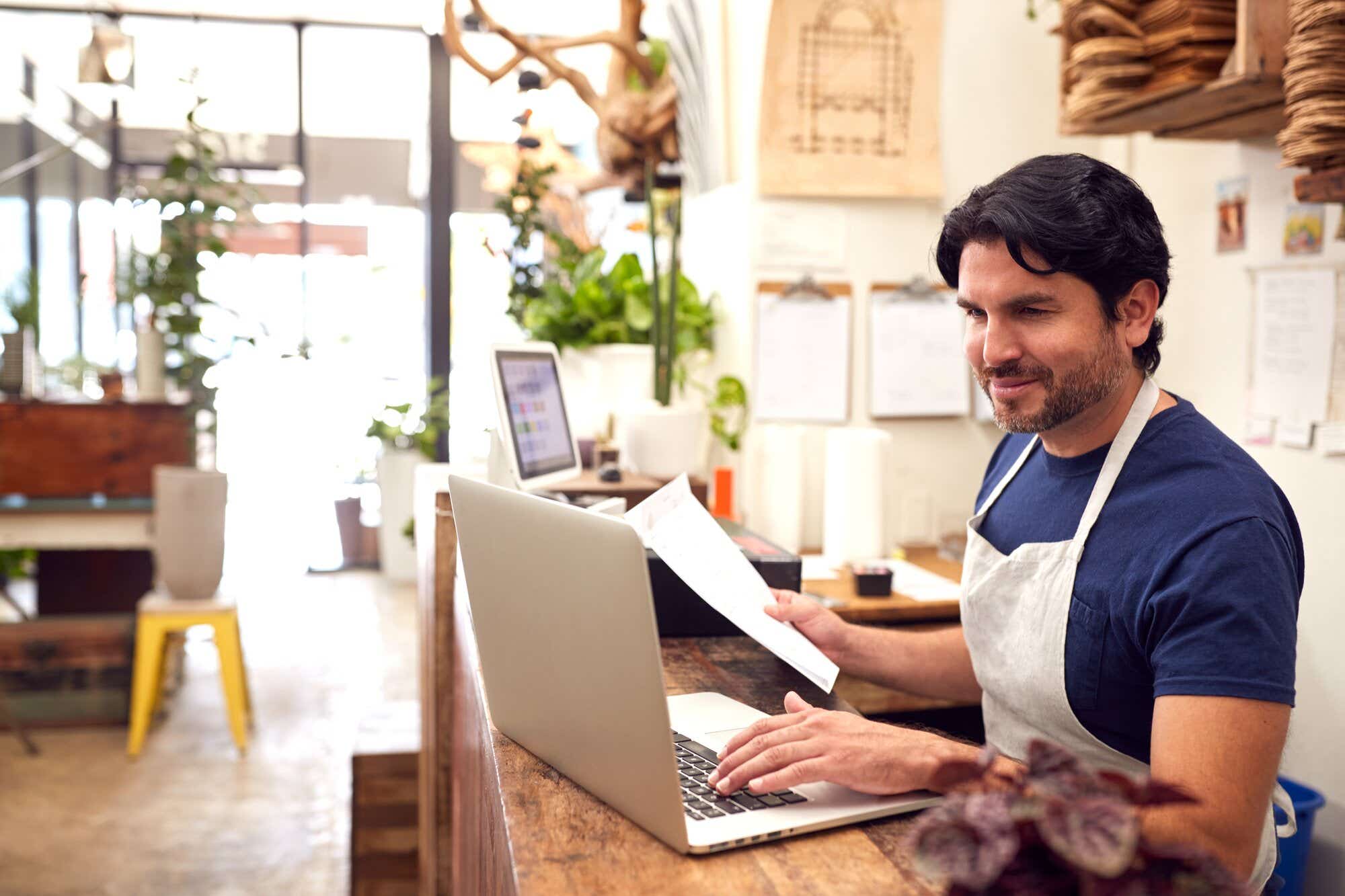 Business owner adding information from a document onto their laptop